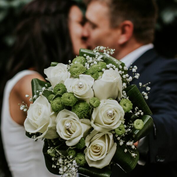 A couple embracing with a focus on a white rose and green floral wedding bouquet.