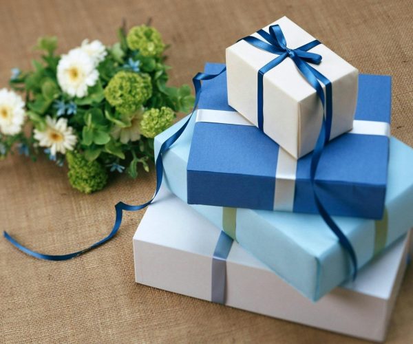 Three beautifully wrapped gift boxes with blue ribbons arranged beside a floral bouquet.